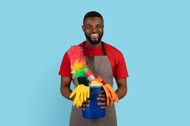 Foto retrato de limpeza de primavera de um cara de faxineiro preto sorridente segurando uma cesta de detergentes