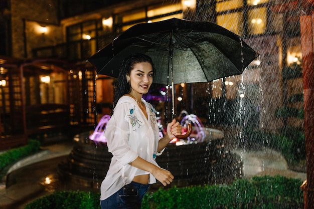 Retrato de linda jovem andando com guarda-chuva sob chuva