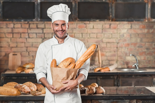 Retrato, de, macho, padeiro, segurando, loaf, de, pães, em, sacola papel