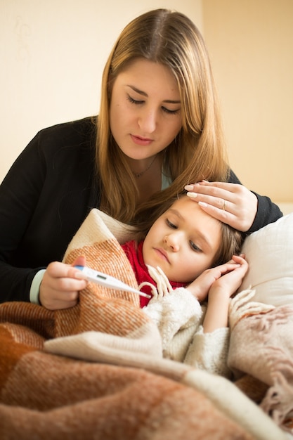 Retrato de mãe carinhosa medindo a temperatura da filha doente com termômetro digital