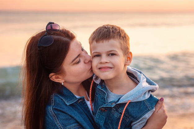 Retrato de mãe caucasiana beija seu filho sorridente no cheak ao fundo é o mar o conceito