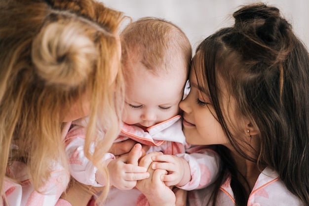 Retrato de mãe com duas filhas na sala branca com o mesmo pijama rosa, olhar de família