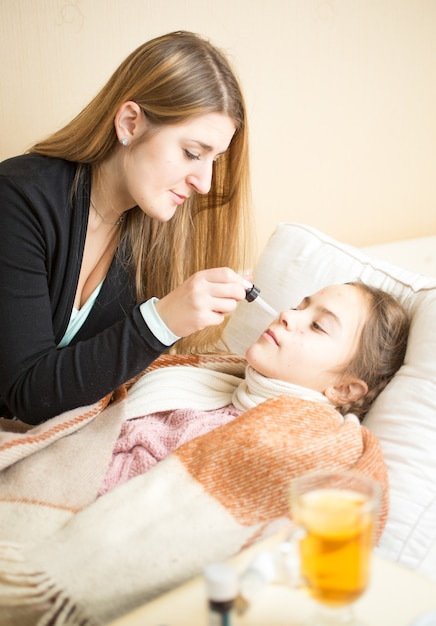 Retrato de mãe dando remédios nasais para filha doente deitada na cama