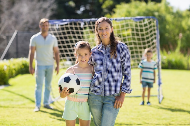 Retrato de mãe e filha em pé com futebol no parque