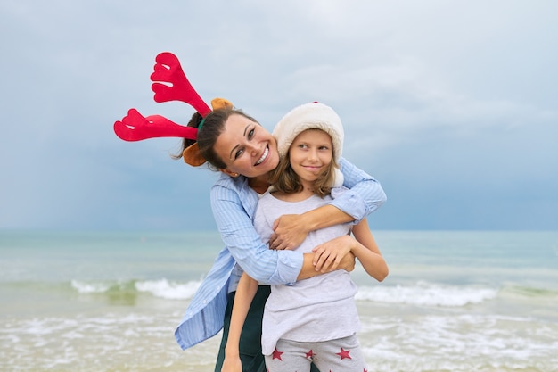 Retrato de mãe e filha felizes abraçando na praia com orelhas de rena