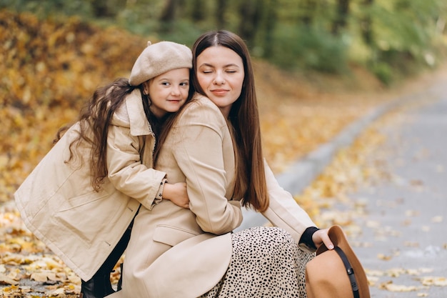 Retrato de mãe e filha felizes passando tempo juntas no parque outono com folhas amarelas caindo