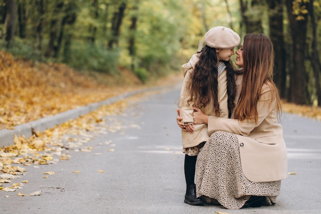 Retrato de mãe e filha felizes passando tempo juntas no parque outono com folhas amarelas caindo