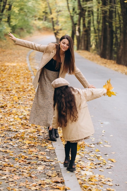 Retrato de mãe e filha felizes passando tempo juntas no parque outono com folhas amarelas caindo