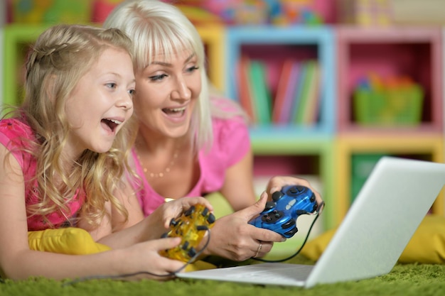 Retrato de mãe e filha sorridentes usando laptop jogando videogame