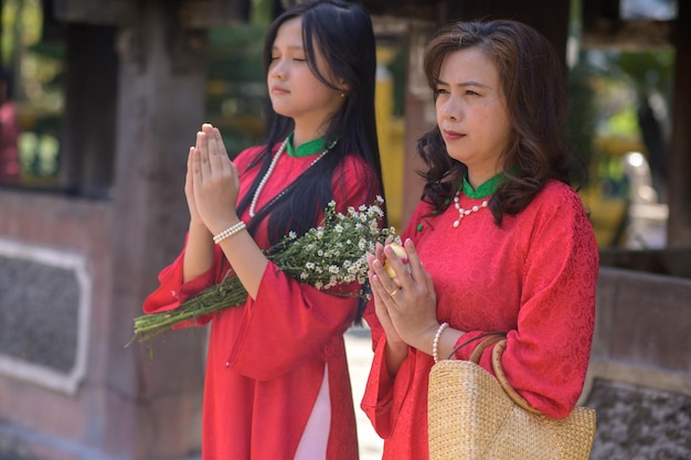 Retrato de mãe e filha vietnamitas em vestido vermelho Ao Dai visitam o pagode no feriado de Tet