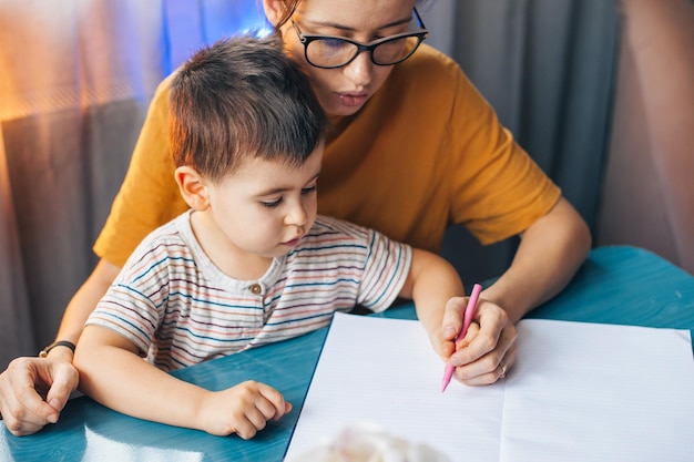 Retrato de mãe e filho sentados à mesa de mãos dadas desenhando em casa educ distante