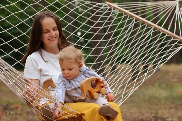 Retrato de mãe e filho sorridentes felizes relaxando na rede na floresta mãe e filha jogando brinquedos ecológicos de madeira passando o dia de verão curtindo a natureza e o ar fresco