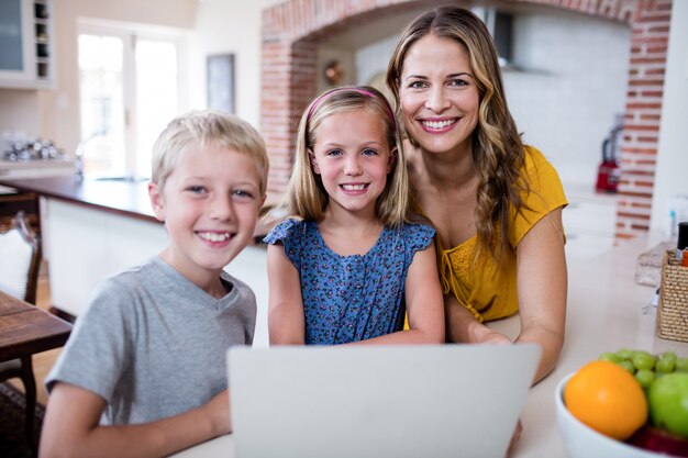 Retrato de mãe e filhos usando o laptop na cozinha