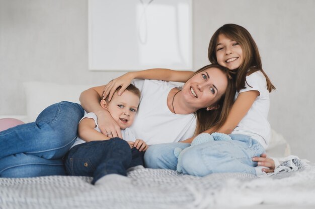 Retrato de mãe feliz e filhos abraçados na cama em casa