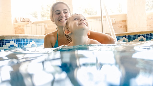 Retrato de mãe feliz e sorridente com filho de 3 anos de idade, nadando na piscina no ginásio. Família relaxando, se divertindo e brincando na água