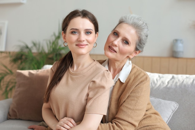 Retrato de mãe idosa e filha madura, abraçando-se em casa. Feliz mãe sênior e filha adulta, abraçando com amor no sofá.