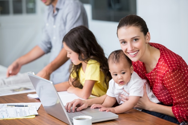 Retrato de mãe sorridente trabalhando no laptop com bebê