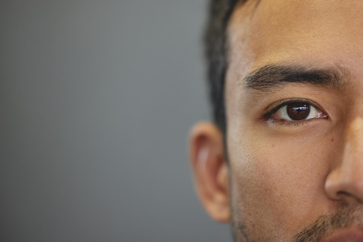 Foto retrato de maquete e meio-olhos de um homem isolado em um fundo cinza no estúdio asiático sério e rosto em close de uma pessoa com espaço para expressão com aparência bonita e um olho jovem em um pano de fundo