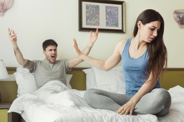 Retrato de marido e mulher discutindo um com o outro, sentados na cama