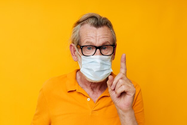 Retrato de máscara médica de homem sênior feliz em um tiro monocromático de camisa amarela