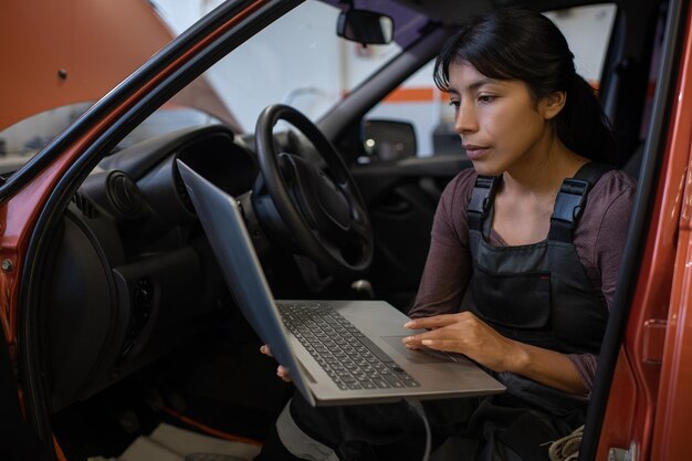 Retrato de mecânico de automóveis feminino usando laptop enquanto inspecionava o veículo na oficina de automóveis, copie o espaço