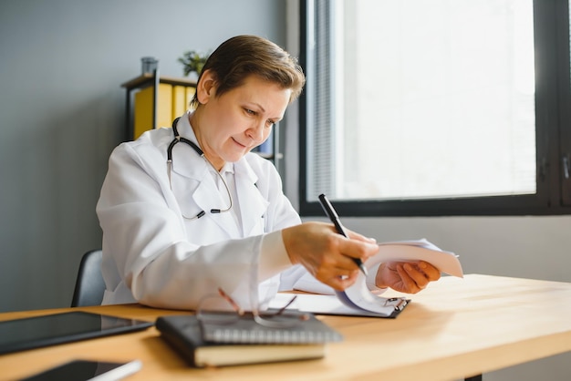 Retrato de médica de meia idade está vestindo um jaleco branco com um estetoscópio em volta do pescoço