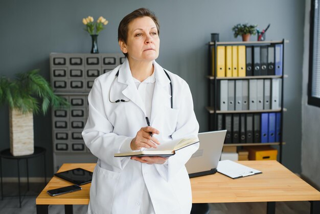 Retrato de médica de meia idade está vestindo um jaleco branco com um estetoscópio em volta do pescoço