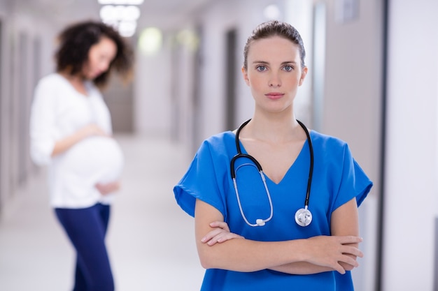 Retrato de médica em pé com os braços cruzados no corredor