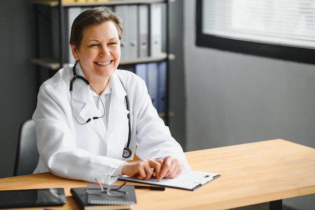 Retrato de médica madura de jaleco branco no local de trabalho