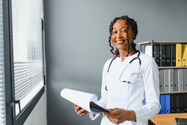 Retrato de médica sorridente usando jaleco branco e estetoscópio no consultório do hospital