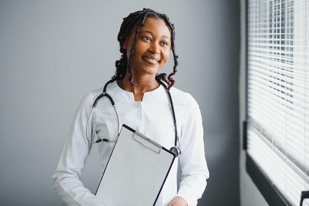 Retrato de médica sorridente usando jaleco branco e estetoscópio no consultório do hospital