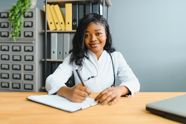 Retrato de médica sorridente usando jaleco branco e estetoscópio no consultório do hospital