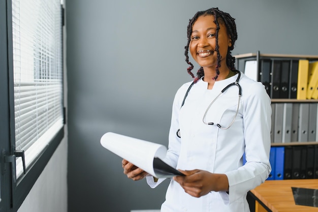 Foto retrato de médica sorridente vestindo jaleco branco com estetoscópio no escritório do hospital