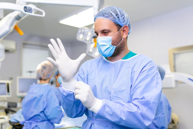 Retrato de médico cirurgião masculino colocando luvas médicas em pé na sala de operação Cirurgião na moderna sala de cirurgia