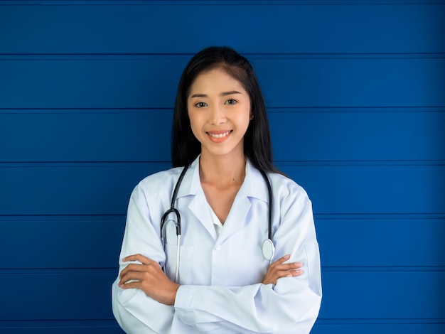 Retrato de médico de mulher asiática sorridente em pé sobre fundo azul de madeira no consultório médico no hospital ou clínica Médica jovem asiática confiante com estetoscópio olhando para a câmera