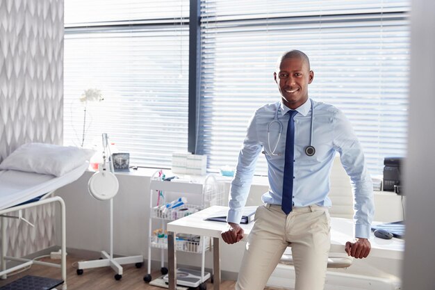 Retrato de médico masculino sorridente com estetoscópio em pé pela mesa no escritório
