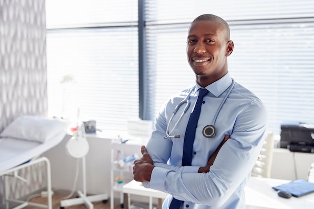 Retrato de médico masculino sorridente com estetoscópio em pé pela mesa no escritório