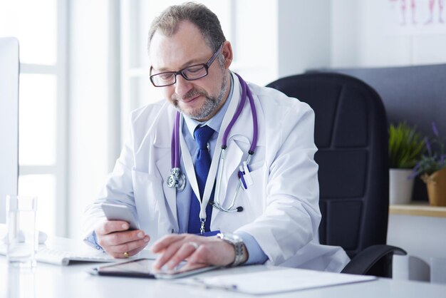 Retrato de médico sênior no escritório sentado na mesa