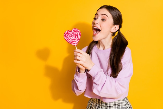 Retrato de menina adolescente alegre e positiva tentando morder um doce em forma de coração
