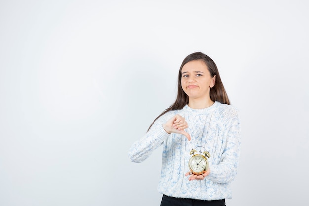 Retrato de menina adolescente em suéter segurando o relógio despertador.