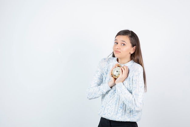 Retrato de menina adolescente em suéter segurando o relógio despertador.