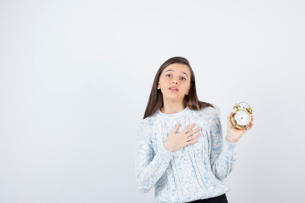 Retrato de menina adolescente em suéter segurando o relógio despertador.