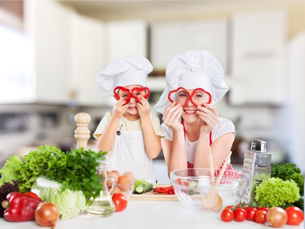 Retrato de menina adorável e sua mãe cozinhando juntos e se divertindo na cozinha