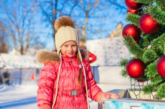 Retrato de menina adorável perto de árvore de Natal na pista de patinação