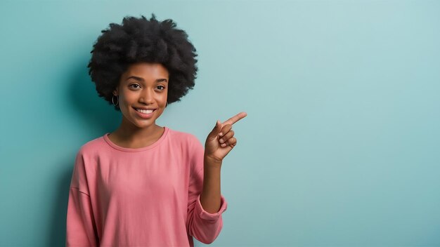 Foto retrato de menina africana sorridente em roupas casuais cor-de-rosa apontando o dedo indicador de lado isolado em azul