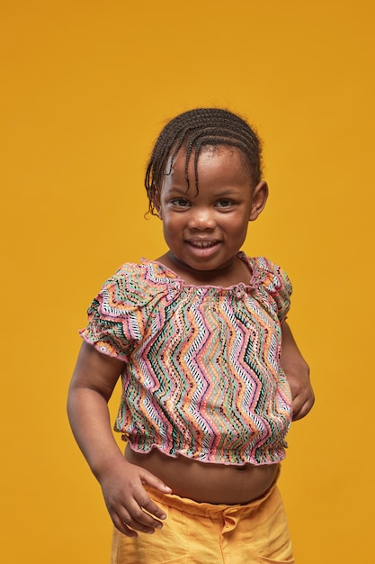 Retrato de menina africana sorrindo para a câmera em pé contra um fundo amarelo