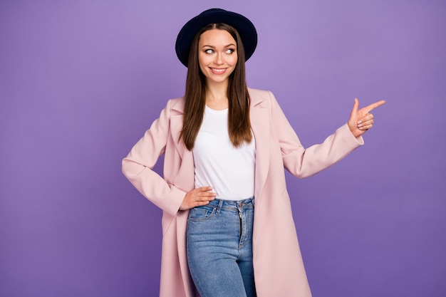 Retrato de menina alegre positiva em roupas de casaco pastel apontar dedo indicador copyspace indicar anúncios promo maneira direta vestir roupa moderna de outono isolada sobre fundo de cor violeta