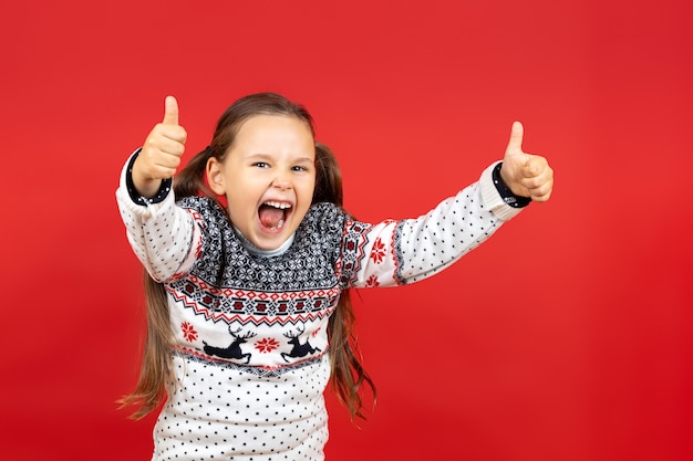 Retrato de menina alegre rindo em suéter de natal branco com renas dando polegares para cima isolado.