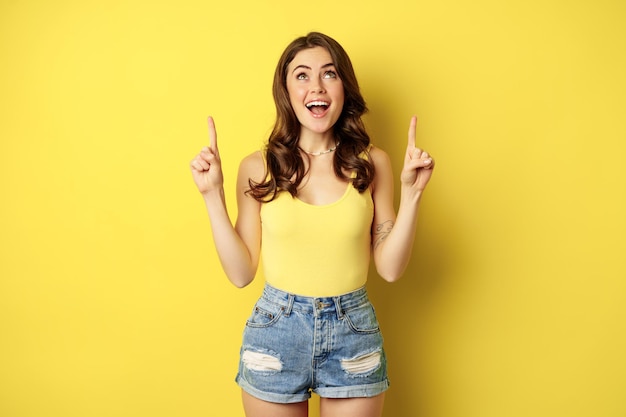 Retrato de menina alegre sorrindo apontando os dedos para cima mostrando o standi de anúncio de verão de texto promocional...