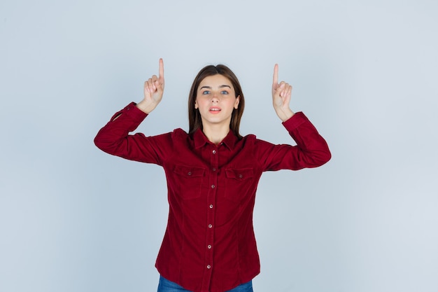 Foto retrato de menina apontando para cima com uma blusa cor de vinho e parecendo confiante